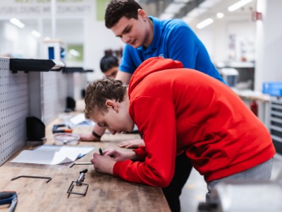 Schüler und Azubis messen Bauteil aus Ein Schüler und ein Azubis messen zusammen am Werktisch ein Bauelement aus